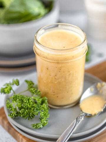 An overview shot of a jar of apple cider vinegar dressing in a jar next to a spoon and parsley on top of grey plates