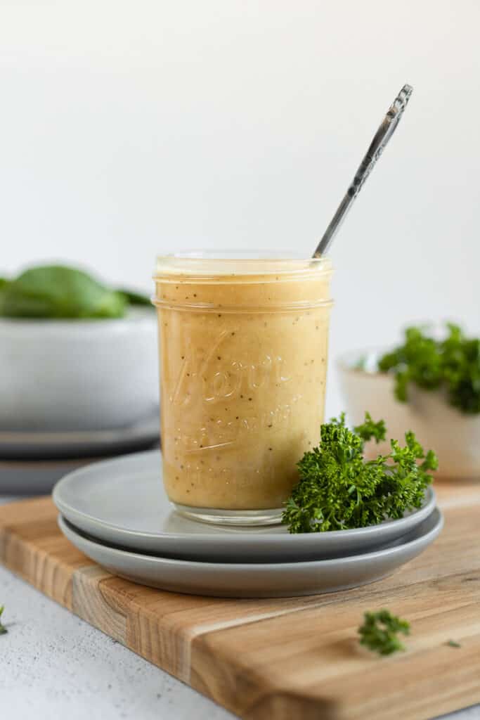 A straight on shot of a jar of apple cider vinegar dressing next to parsley on grey plates and a cutting board.