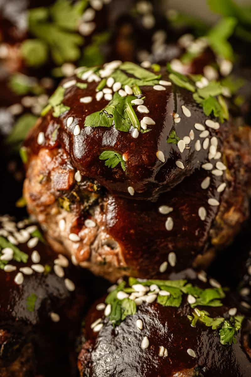A close up view of a bowl of sticky asian meatballs topped with sauce, sesame seeds, and cilantro.