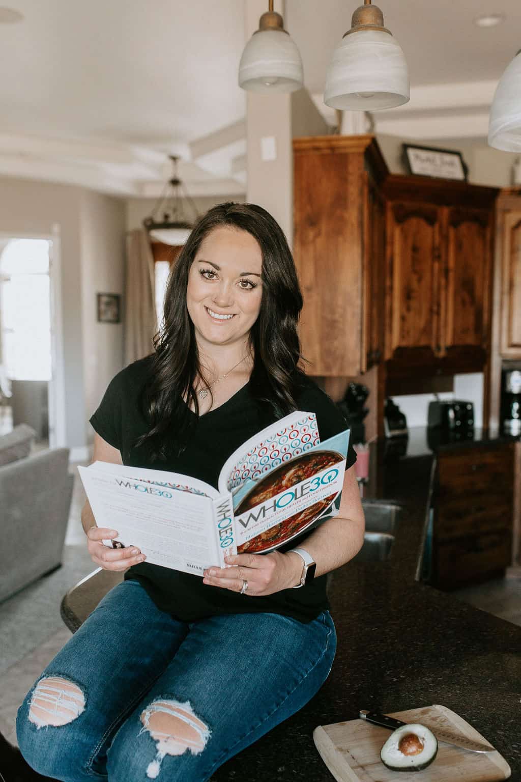 Woman smiling while reading Whole 30 book sitting on kitchen counter