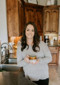 A woman in her kitchen smiling with a cup of coffee