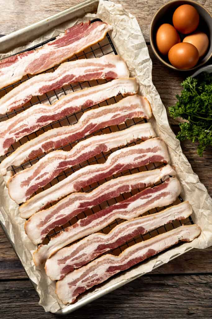 A baking sheet with raw bacon on a wood background