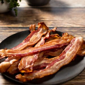 A plate of crispy oven bacon on a wood background next to eggs and parsley