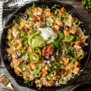 An overview shot of a cast iron skillet filled with nachos and topped with sour cream, guacamole, cilantro, and salsa.