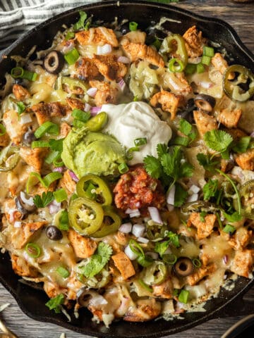 An overview shot of a cast iron skillet filled with nachos and topped with sour cream, guacamole, cilantro, and salsa.