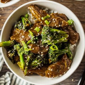 A white bowl of beef and broccoli on a wood background.