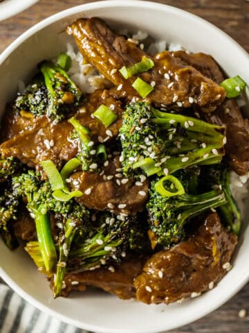 A white bowl of beef and broccoli on a wood background.