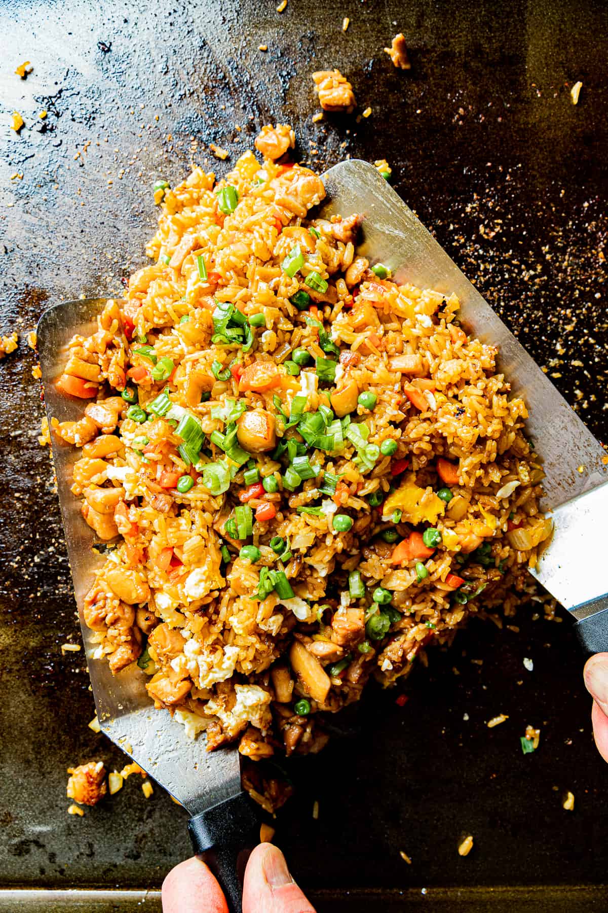 An overview shot of chicken fried rice on a blackstone griddle being tossed by two spatulas.