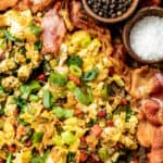 An overview shot of eggs, hashbrowns, and bacon on a baking sheet topped with green onions, salt, and pepper.