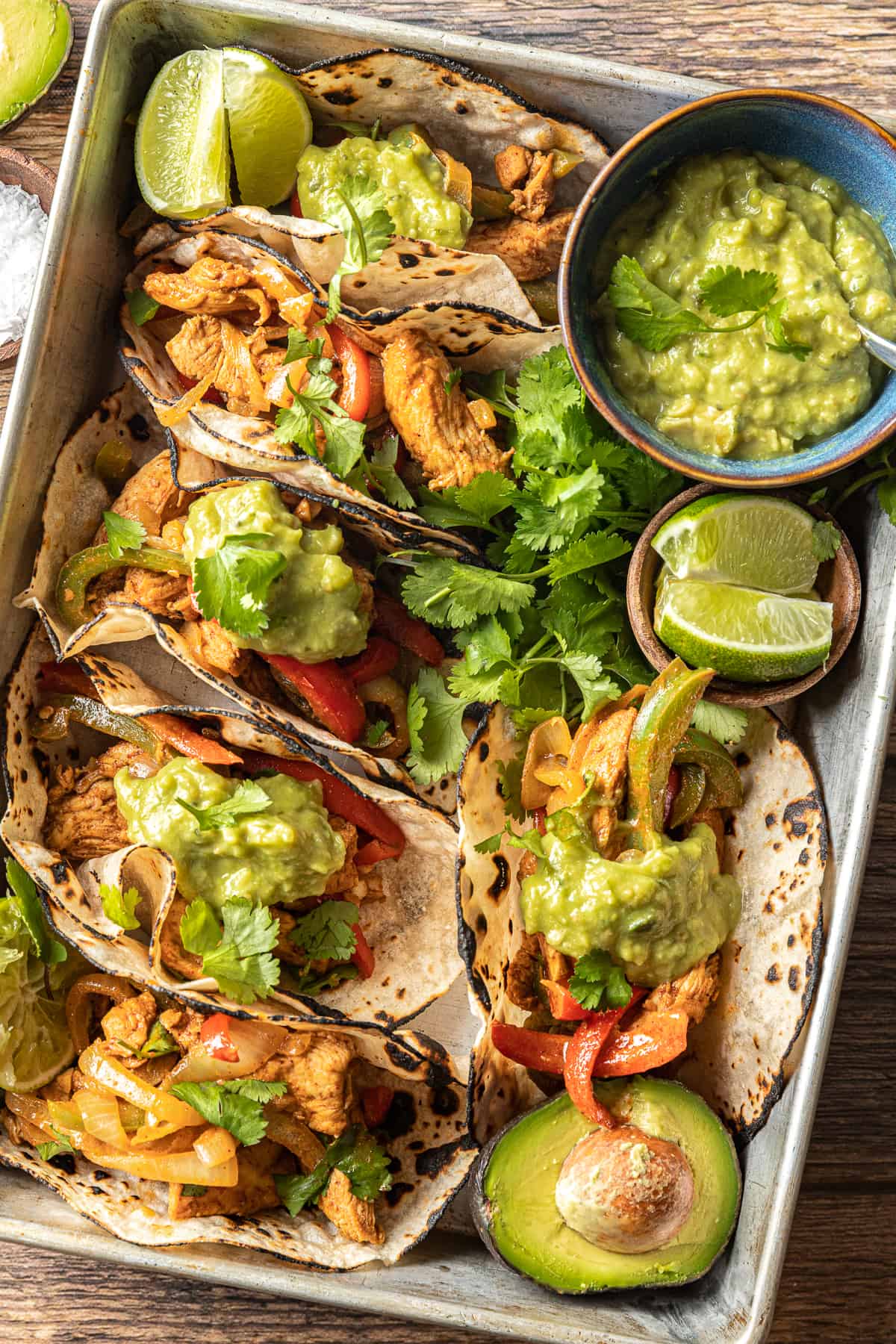 A pan of tacos filled with chicken fajitas and topped with guacamole, cilantro, and lime wedges