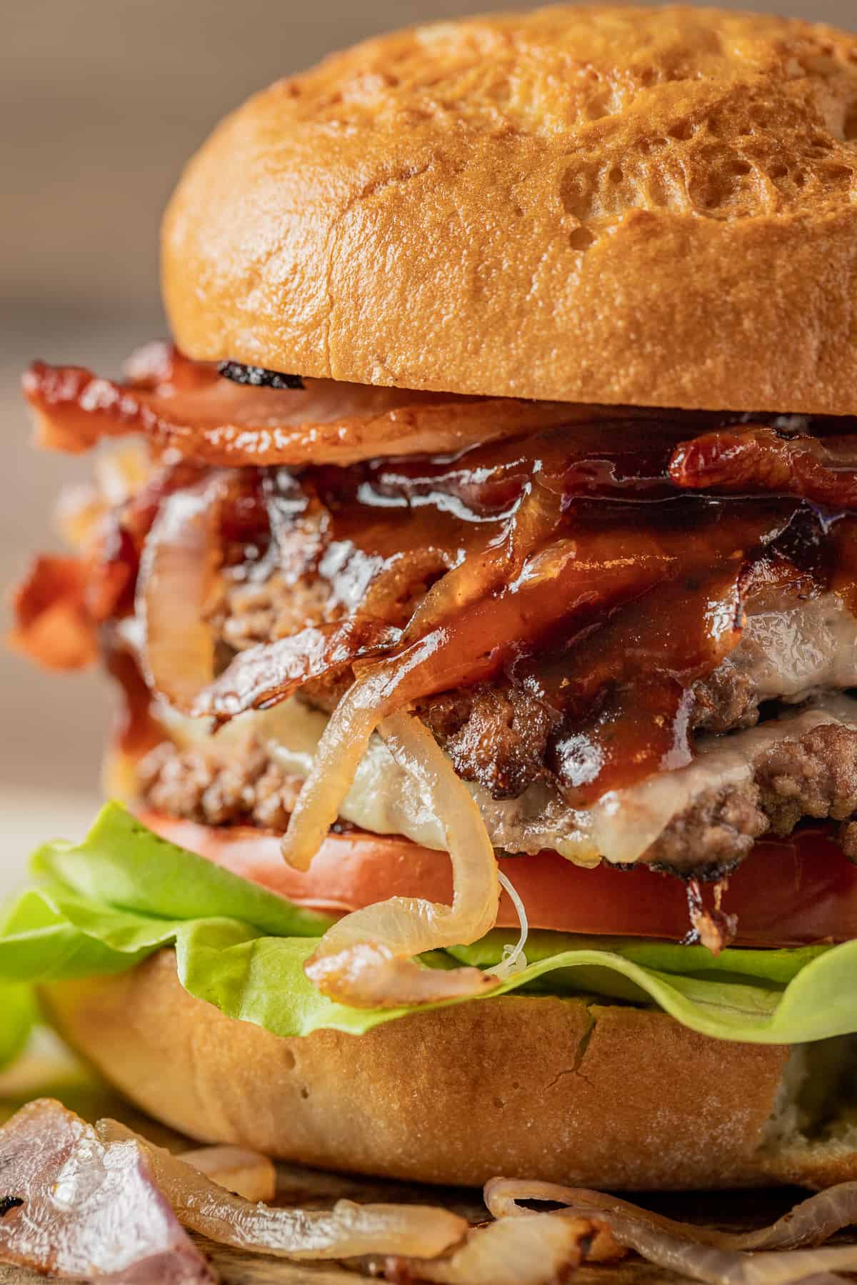 A close up view of two smash burger patties topped with cheese, bbq sauce, onions, and bacon on buns.