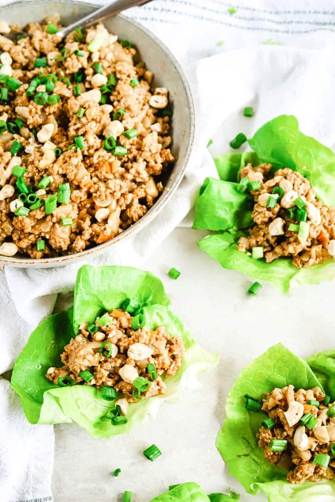 A top view of a bowl of chicken lettuce wrap filling and lettuce wraps