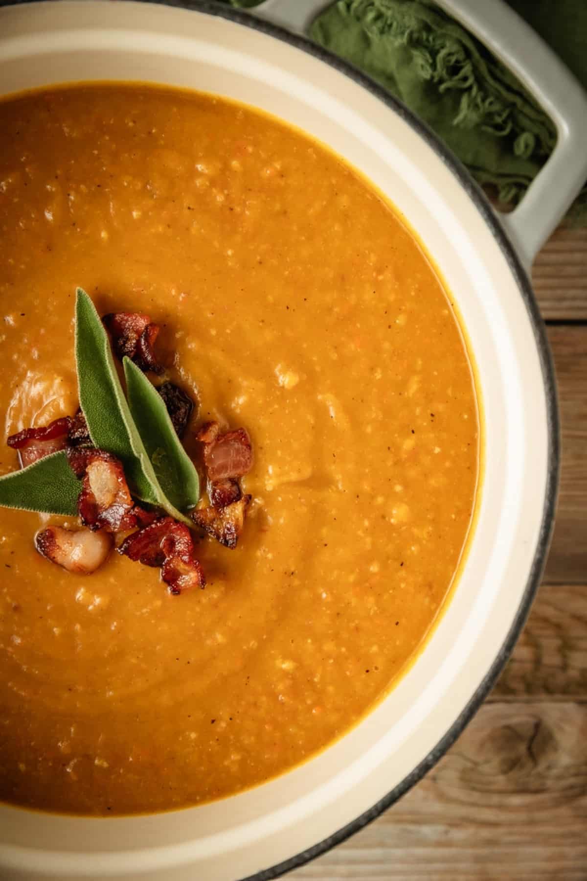 A dutch oven pot filled with butternut squash soup topped with bacon and sage.