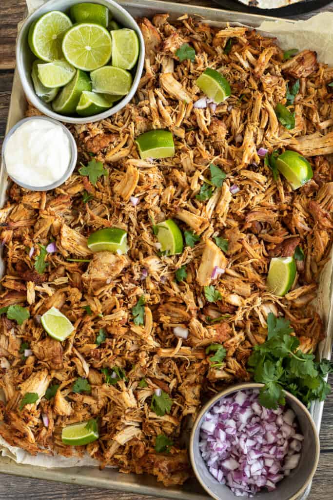 An overview shot of pork carnitas on a pan topped with limes and cilantro