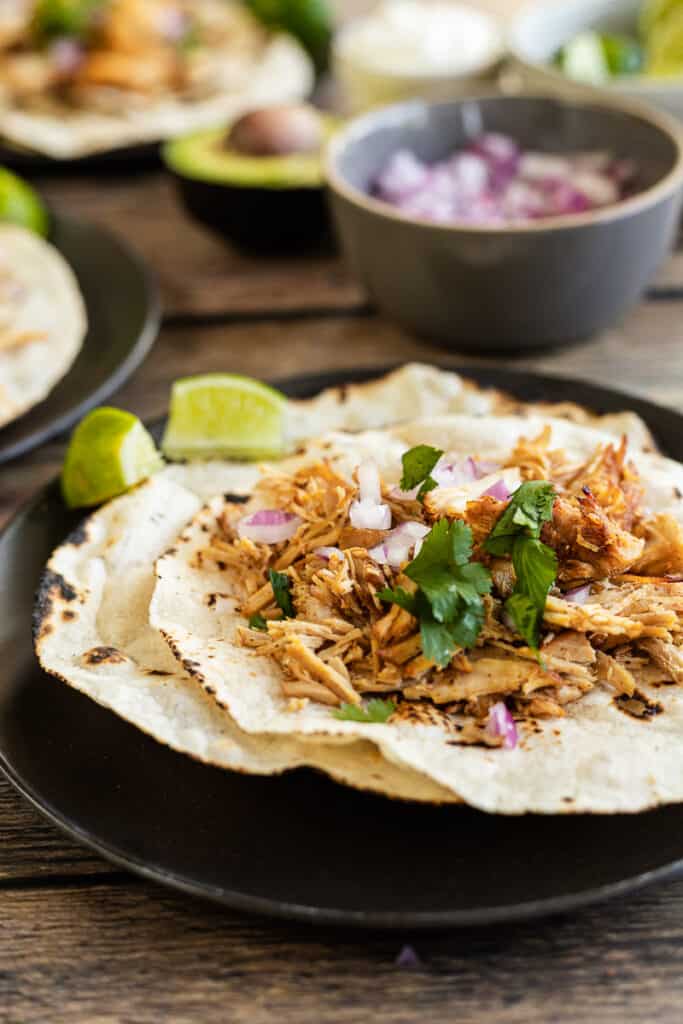 Tortillas on a black plate topped with carnitas, lime, and cilantro