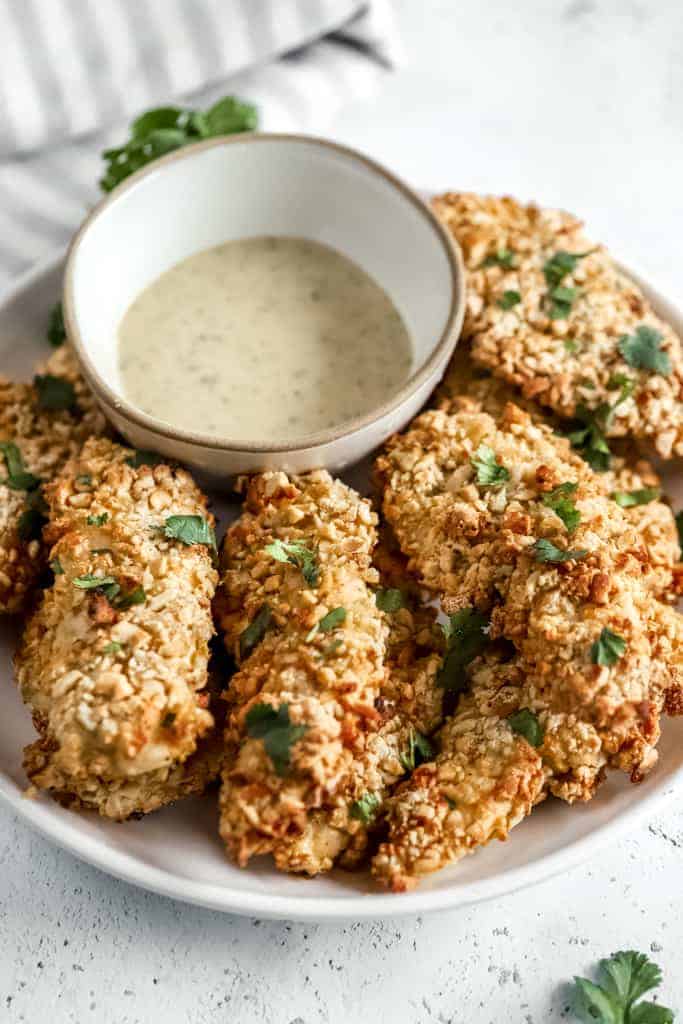 A plate of baked chicken tenders with Whole30 ranch on a grey background