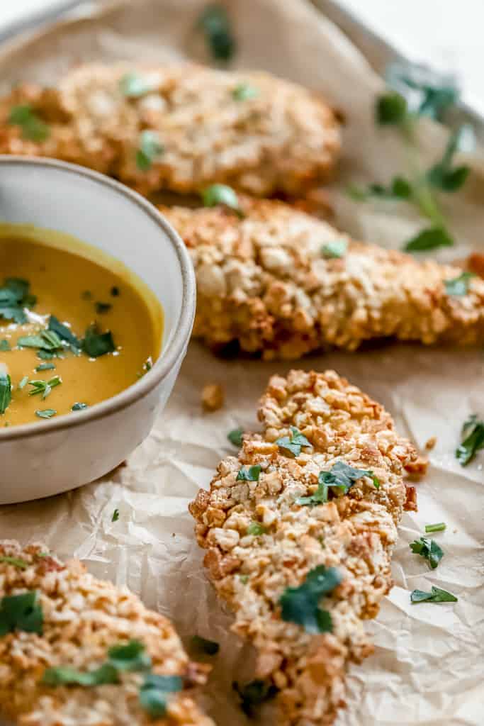A pan of cashew crusted chicken tenders next to a bowl of honey mustard sauce