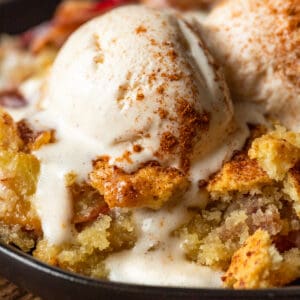 Peach cobbler in a cast iron skillet topped with a scoop of melting ice cream and cinnamon.