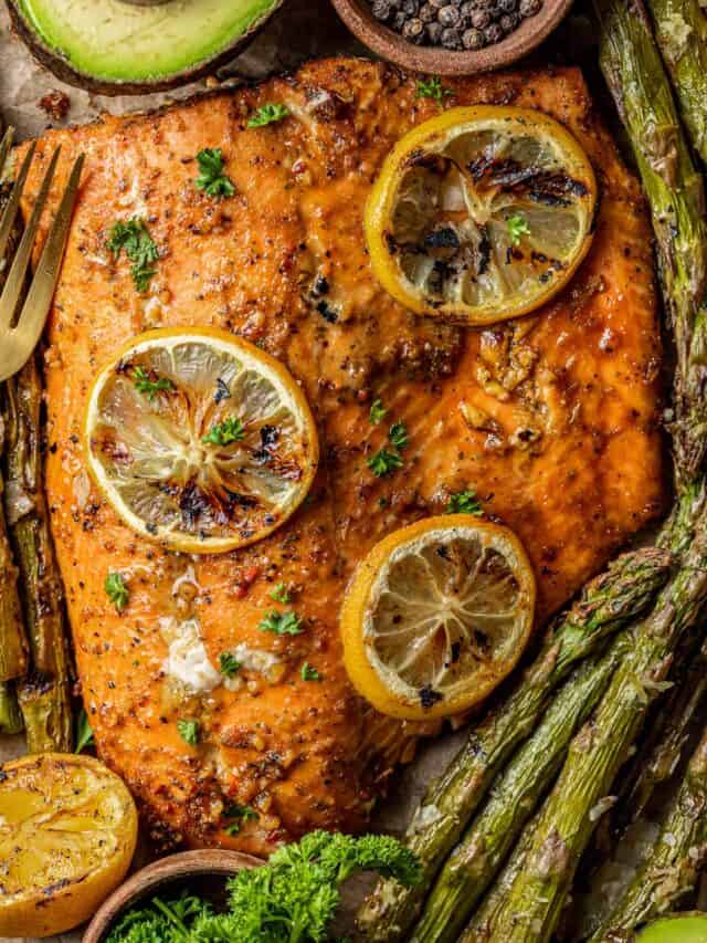 An overview shot of a whole salmon fillet topped with lemon and served with roasted asparagus.