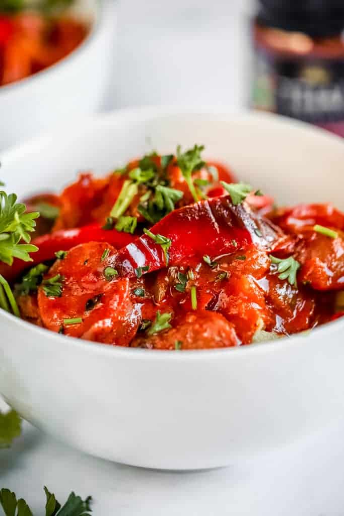 A bowl of thai coconut curry with peppers, onions, and sausage topped with parsley