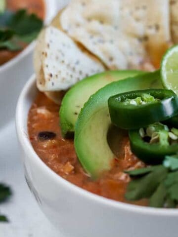 Two bowls of chicken tortilla soup topped with chips, limes, and avocado