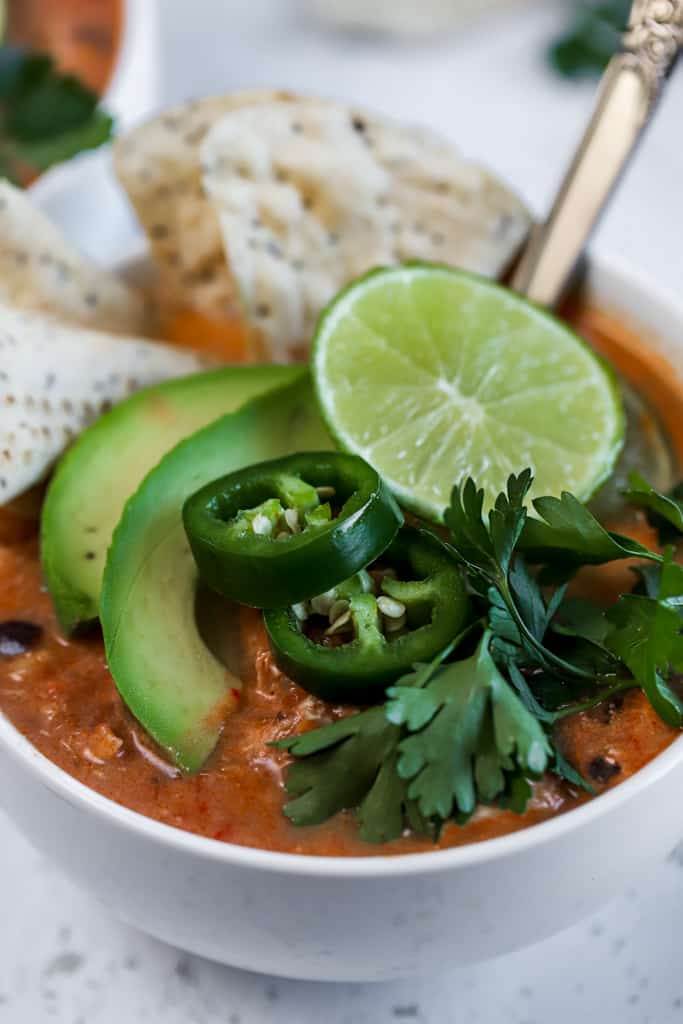 A single bowl of chicken tortilla soup topped with limes, chips, and avocado