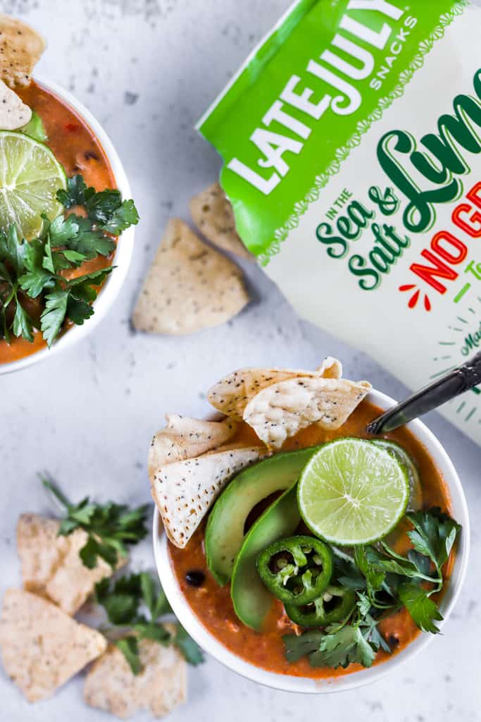 A top view two bowls of creamy chicken tortilla soup next to an open bag of late july chips