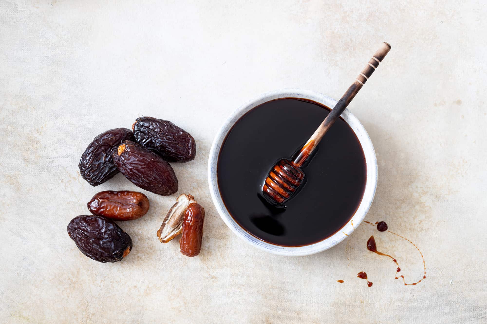 A white bowl of date syrup on a white background next to whole dates.