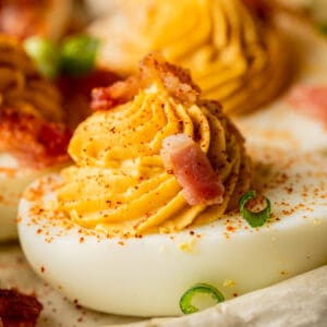 A close up shot of a deviled egg topped with bacon and smoked paprika.