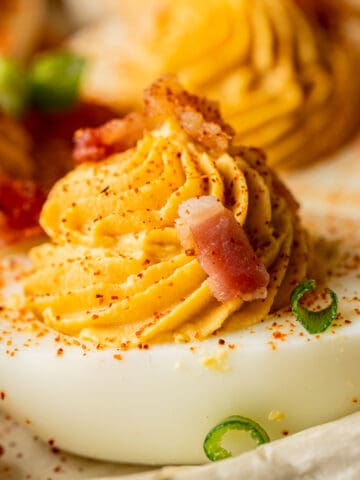 A close up shot of a deviled egg topped with bacon and smoked paprika.