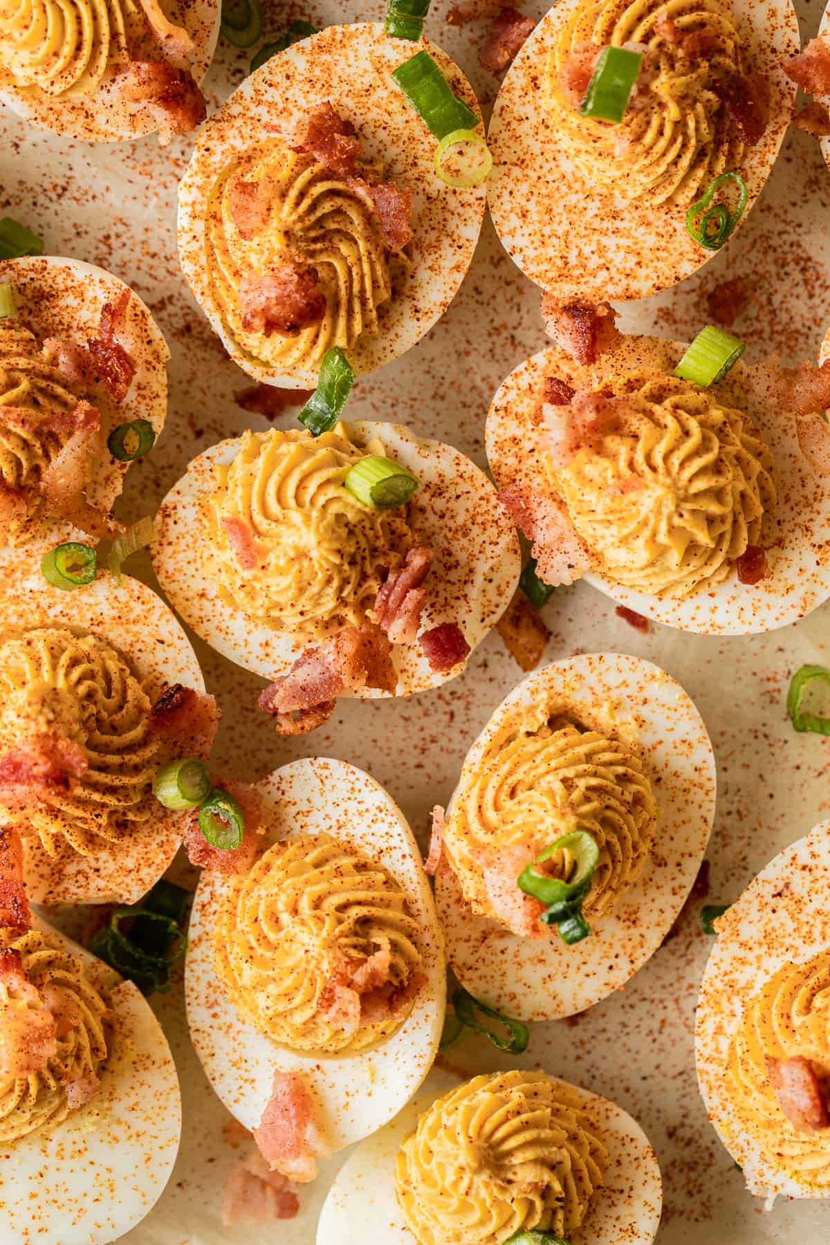 An overview shot of smoked deviled eggs topped with bacon and paprika on a brown background.