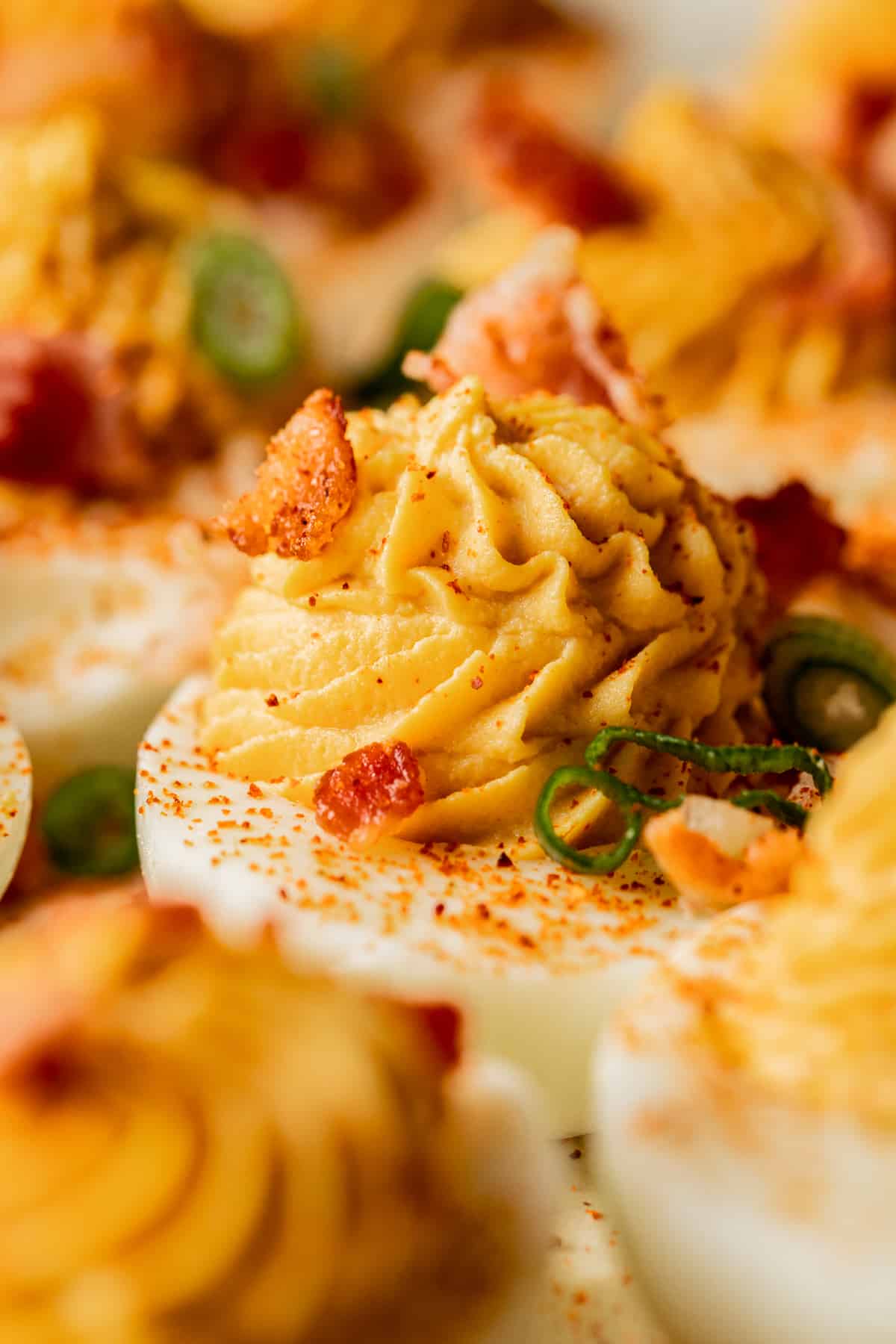 A close up shot of a deviled egg topped with bacon and smoked paprika.