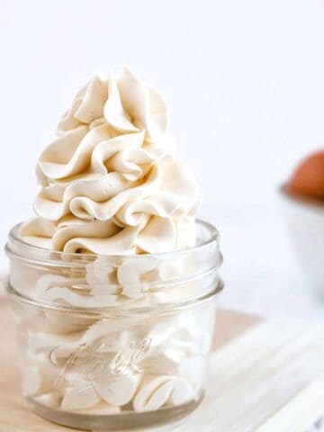 A mason jar with a swiss meringue buttercream swirl in front of a piping bag