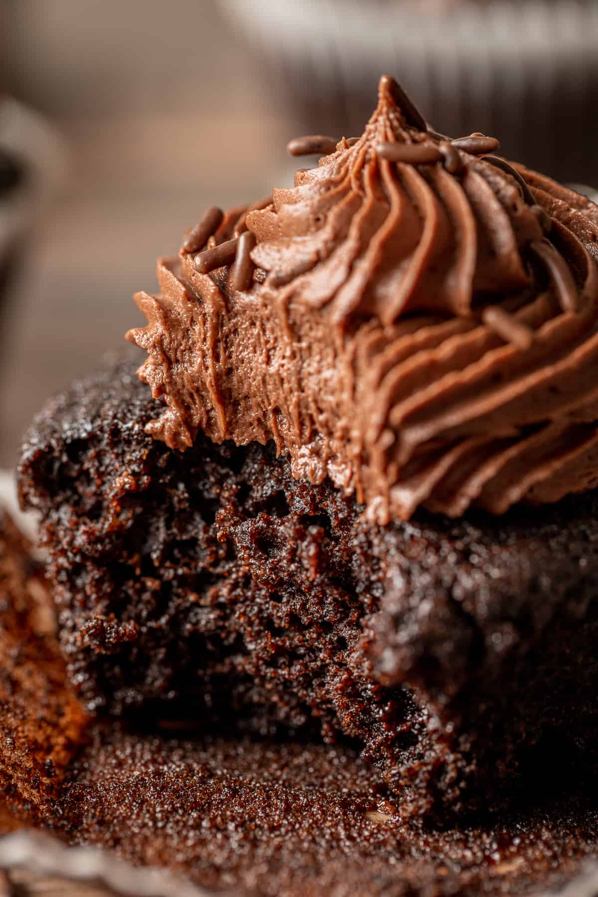 A close up shot of a bite taken out of a chocolate cupcake with chocolate buttercream.