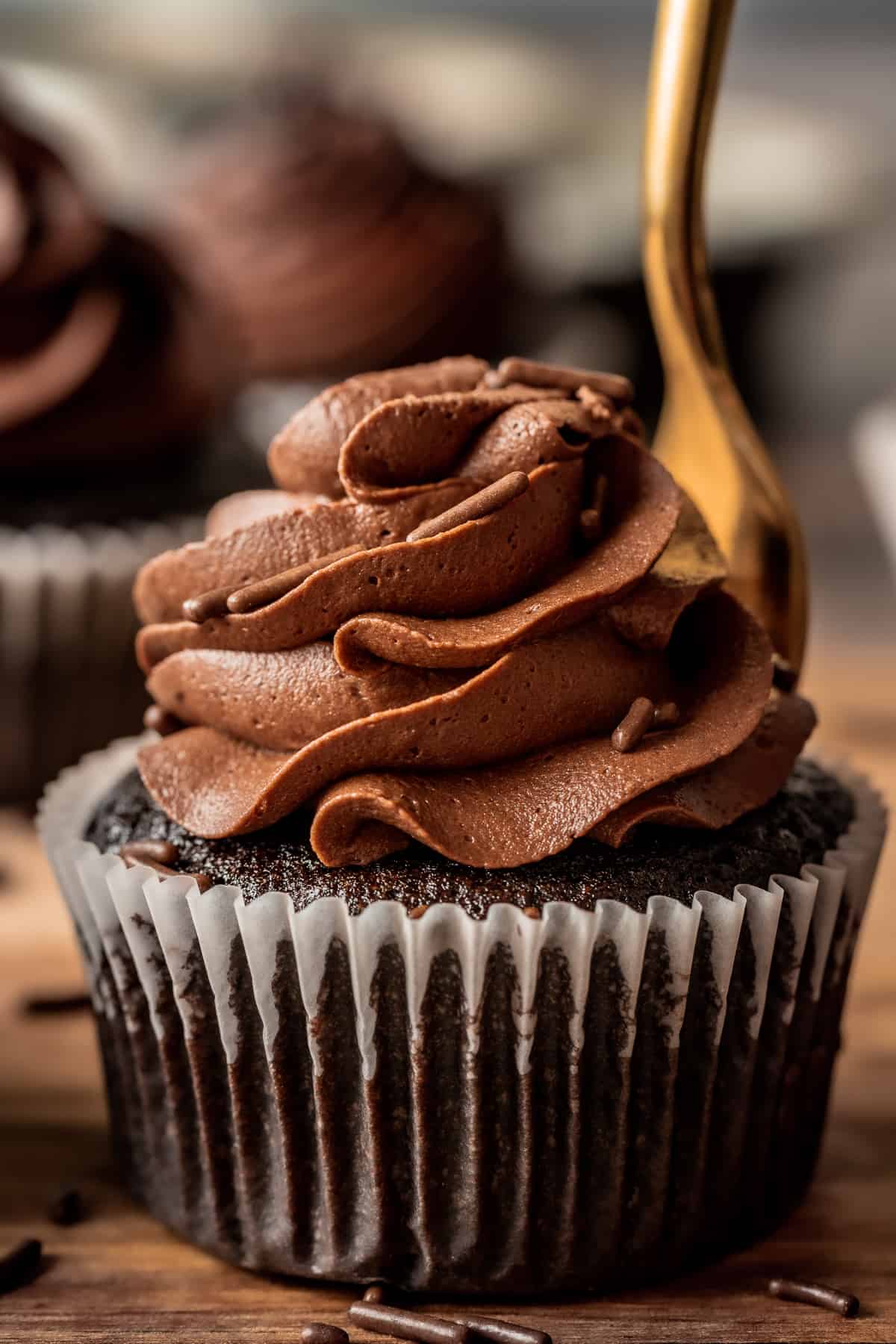 A close up photo of a chocolate cupcake with chocolate buttercream swirl on a wood background.