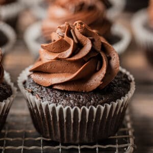 A close up photo of a chocolate cupcake with chocolate buttercream swirl on a wire cooling rack.