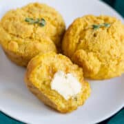 Three cornbread muffins on a white plate topped with a pad of butter.