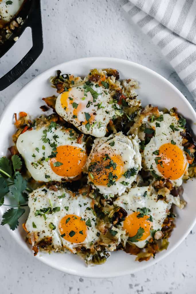 A top shot of a plate of sweet potato hash browns topped with eggs on a white plate