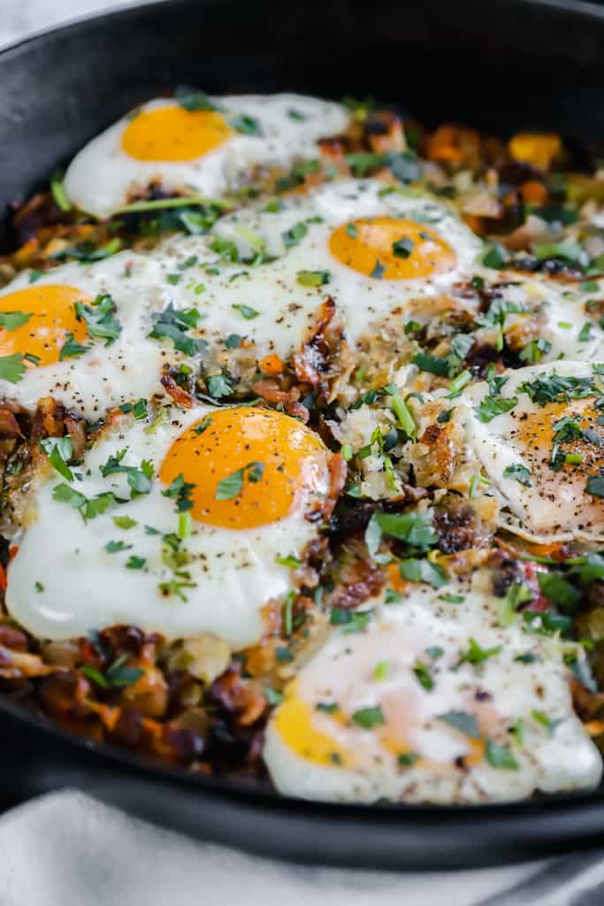Sweet potato hash browns topped with eggs in a cast iron pan