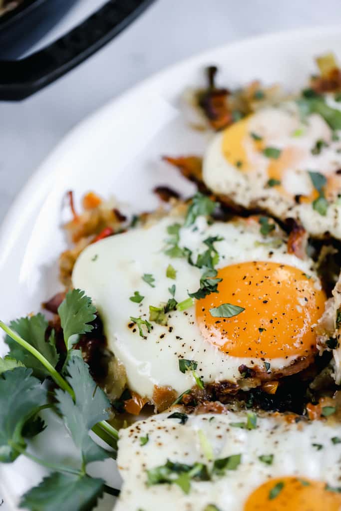 Sweet potato hash browns topped with eggs on a white plate