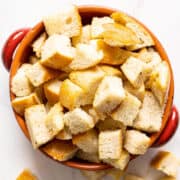 A red bowl of sourdough crouton on a white background.