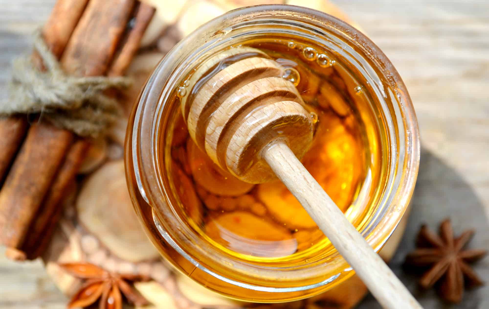 Honey in a glass jar on a wood table with cinnamon sticks.