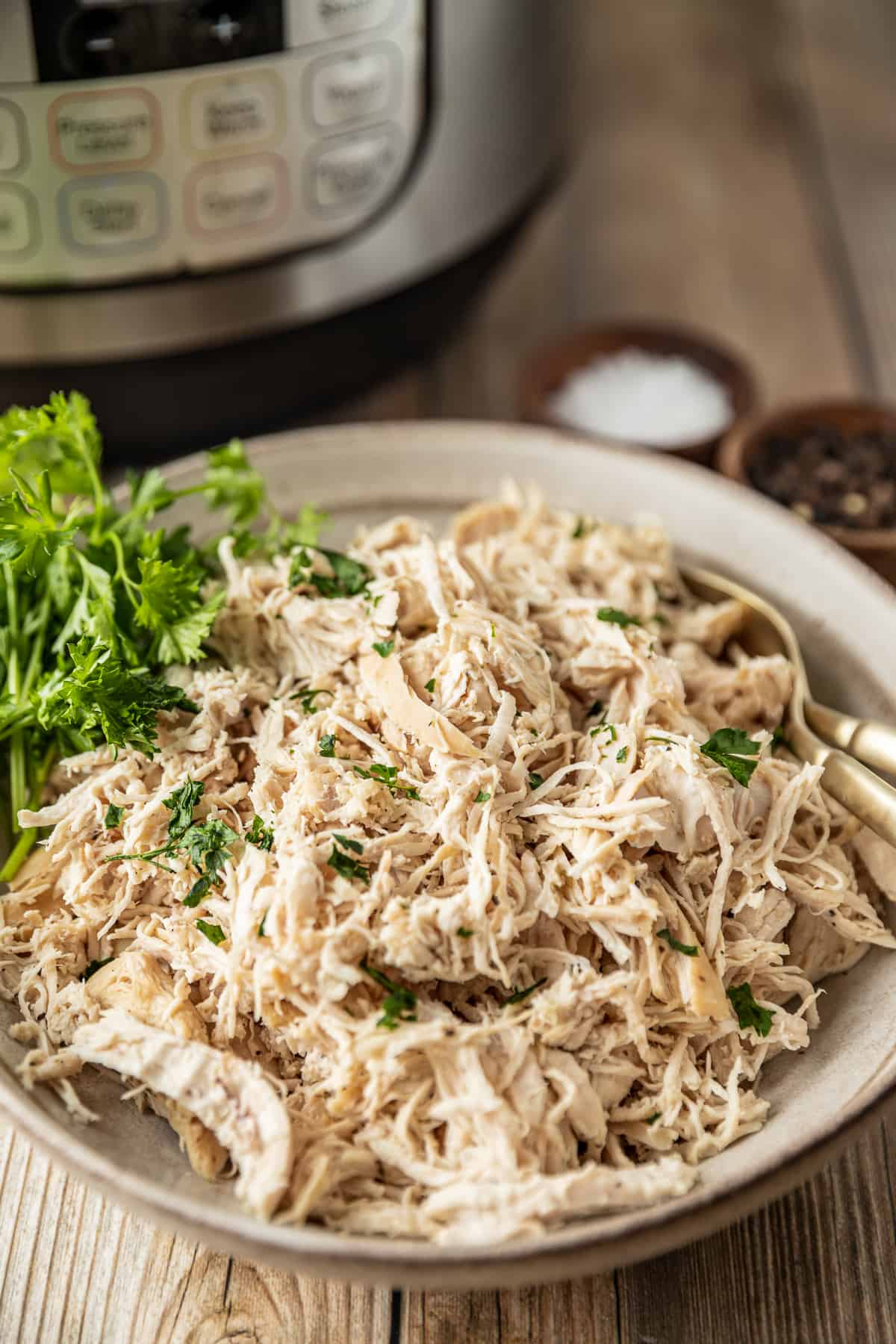 A bowl of shredded chicken in a bowl near an instant pot on a wood background.
