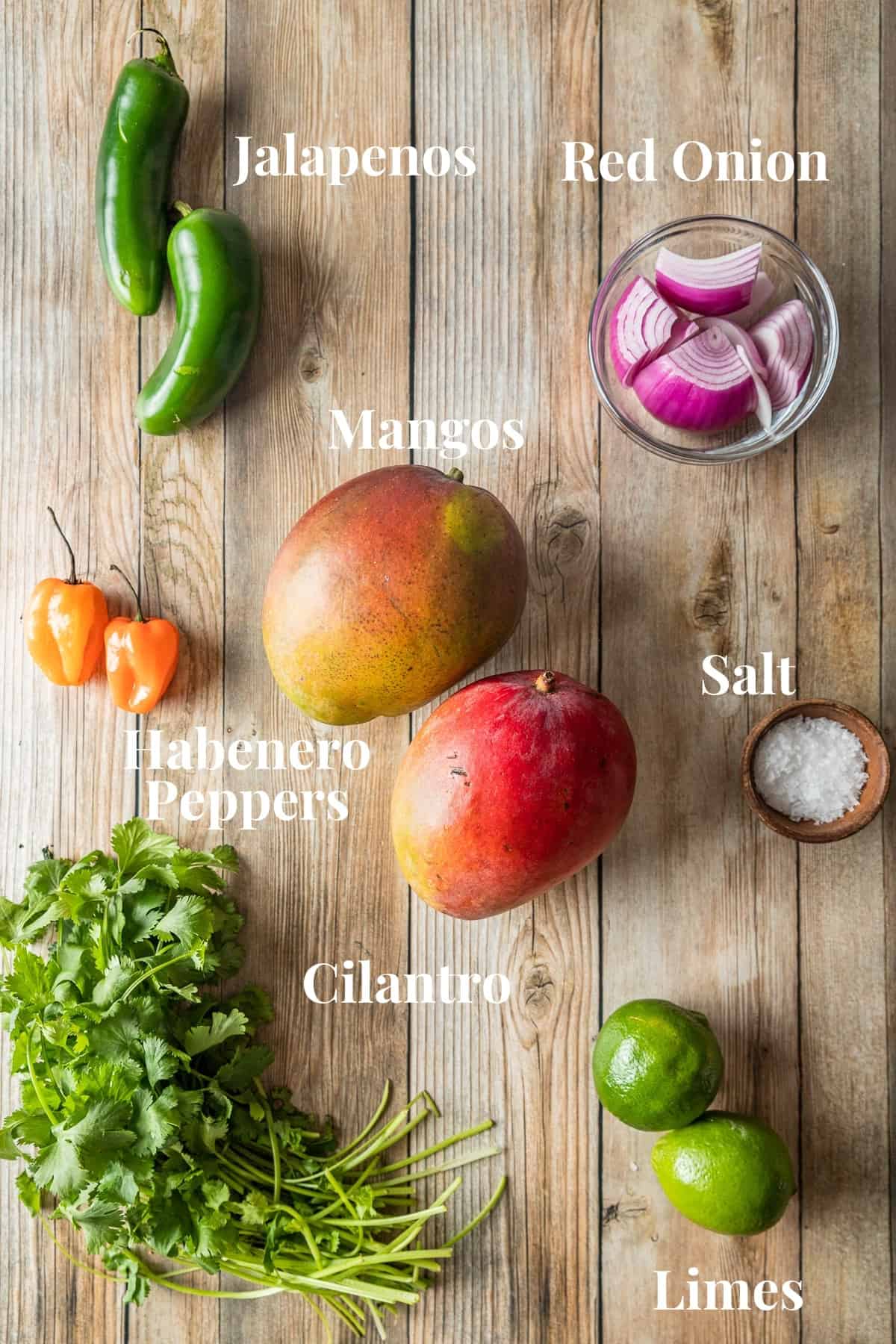A top down view of the ingredients needed for mango salsa on a wood background.