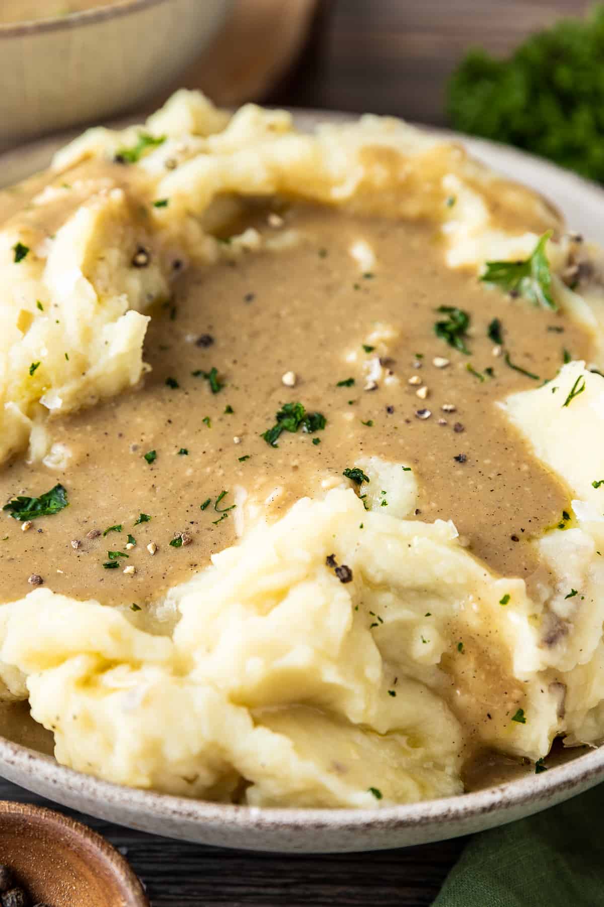 A bowl of mashed sweet potatoes with a pool of gravy and topped with parsley, salt and pepper on a wood background.