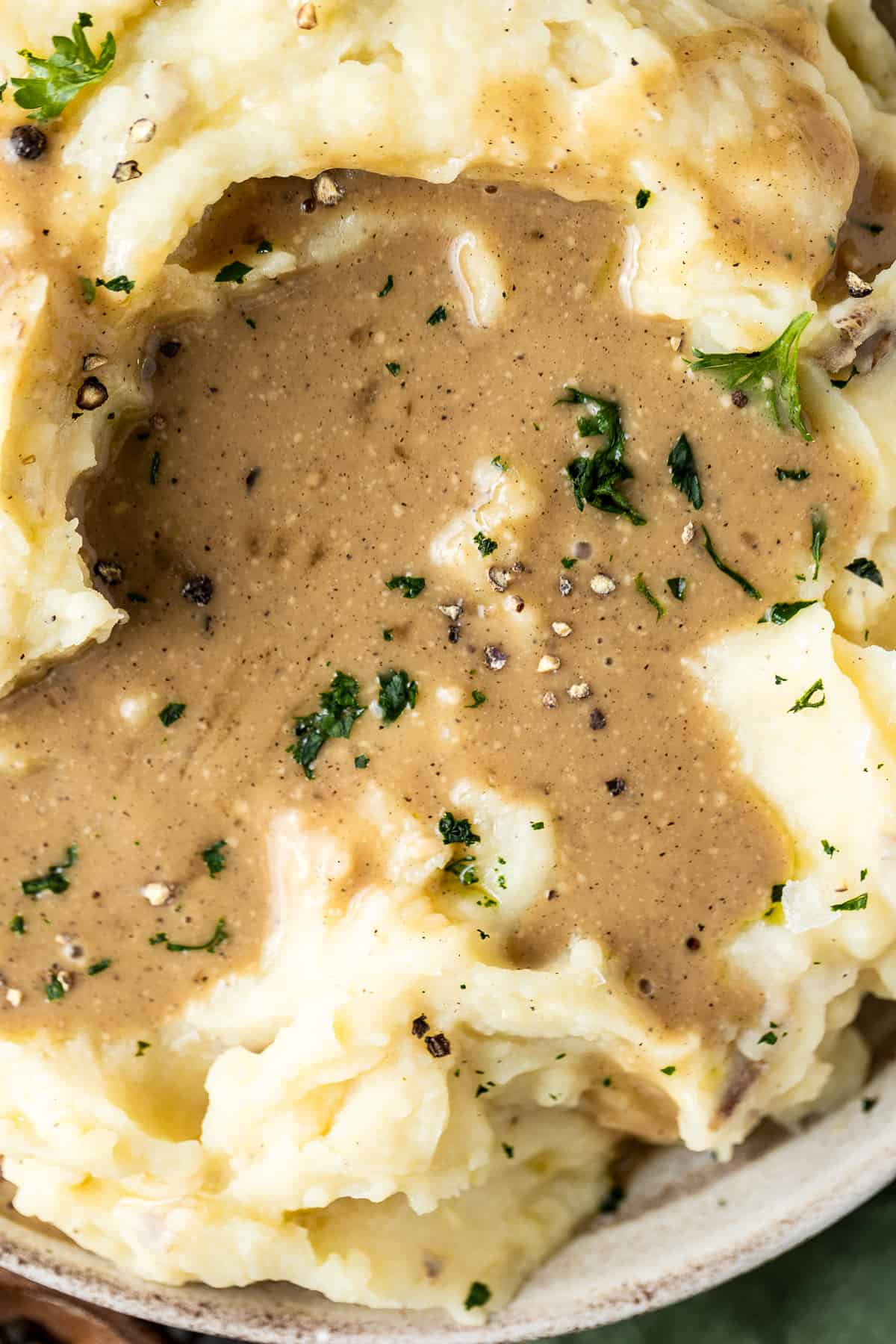 A bowl of mashed sweet potatoes with a pool of gravy and topped with parsley, salt and pepper on a wood background.