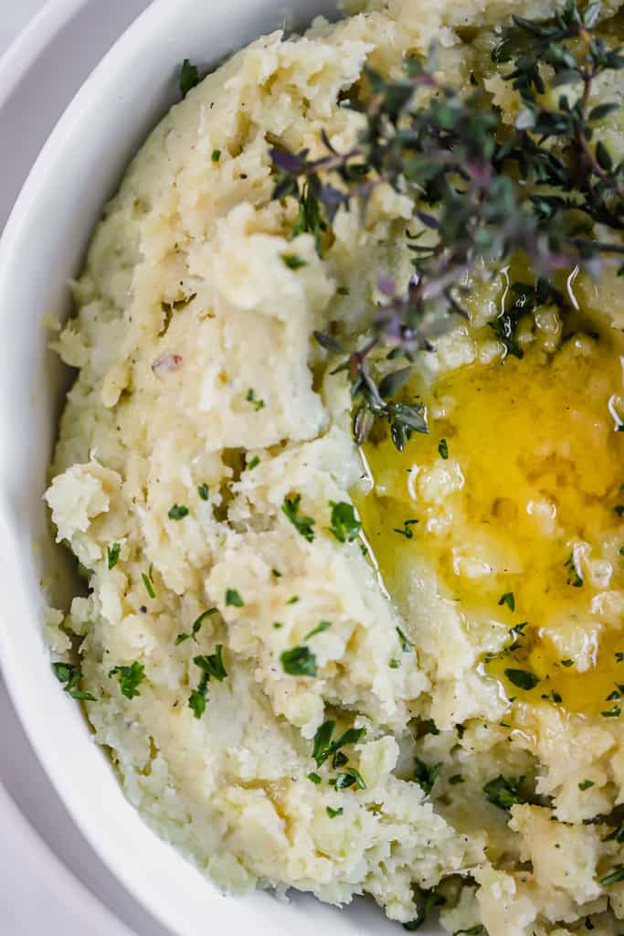 A top view of mashed sweet potatoes in a white bowl topped with herbs and melted ghee