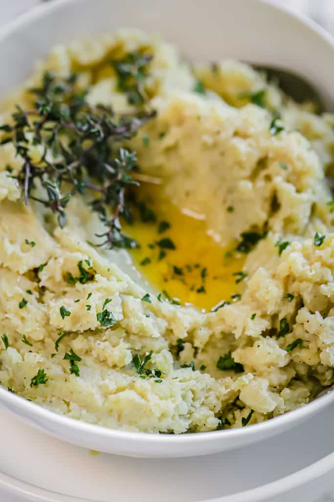 A top view of mashed sweet potatoes in a white bowl topped with herbs and melted ghee