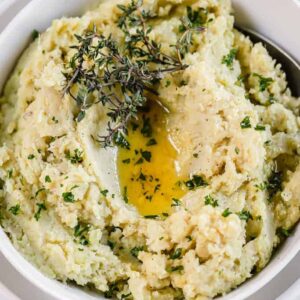 A top view of mashed sweet potatoes in a white bowl topped with herbs and melted ghee