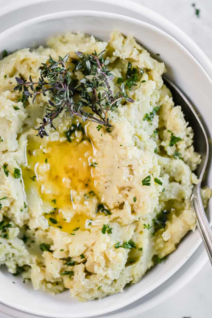 A top view of mashed sweet potatoes in a white bowl topped with herbs and melted ghee